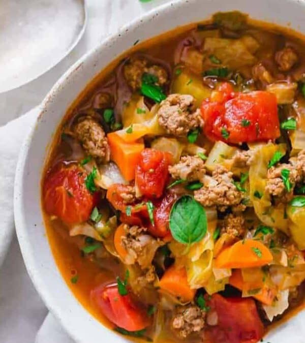 A colorful bowl of vegetable and meat soup garnished with fresh parsley, surrounded by ingredients and a ladle.
