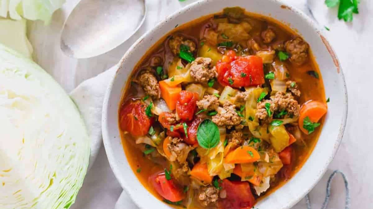 A colorful bowl of vegetable and meat soup garnished with fresh parsley, surrounded by ingredients and a ladle.