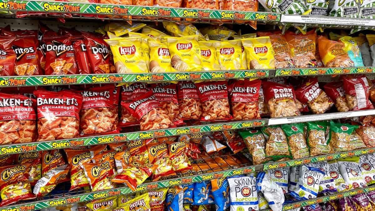 Aisle with assorted brands of snack chips and popcorn on display at a grocery store.