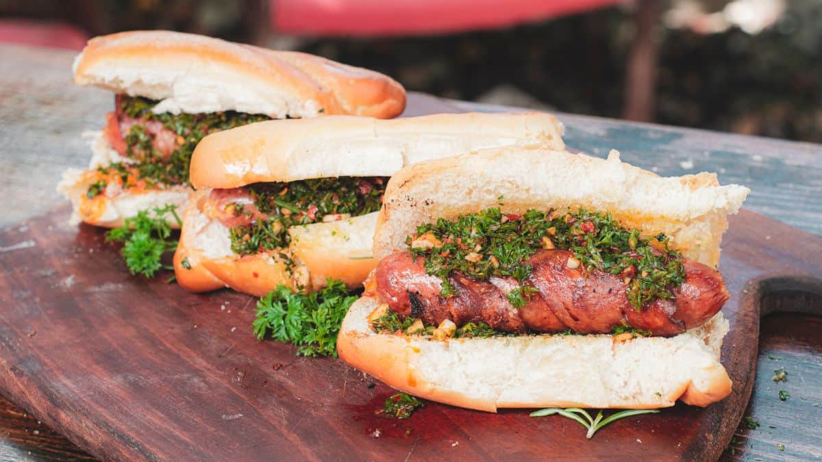 Grilled sausages in crispy bread rolls garnished with herbs on a wooden board.