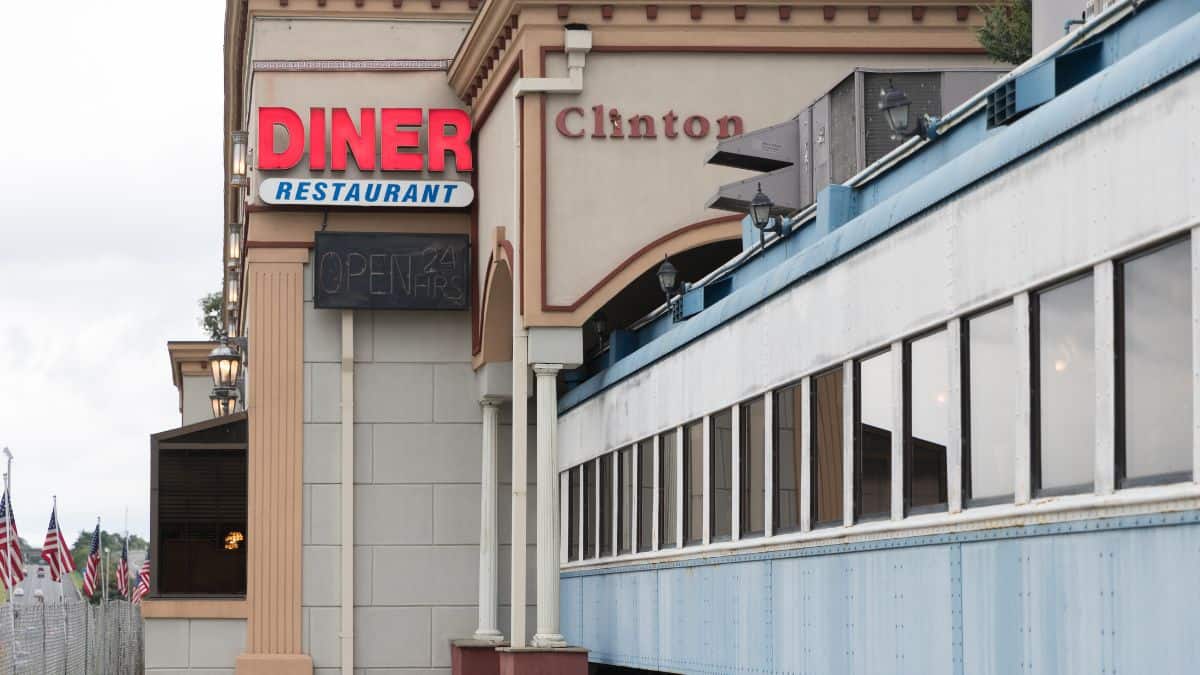 Exterior view of a classic diner named "clinton" featuring a "diner restaurant" sign, open 24 hrs notice, and an american flag.