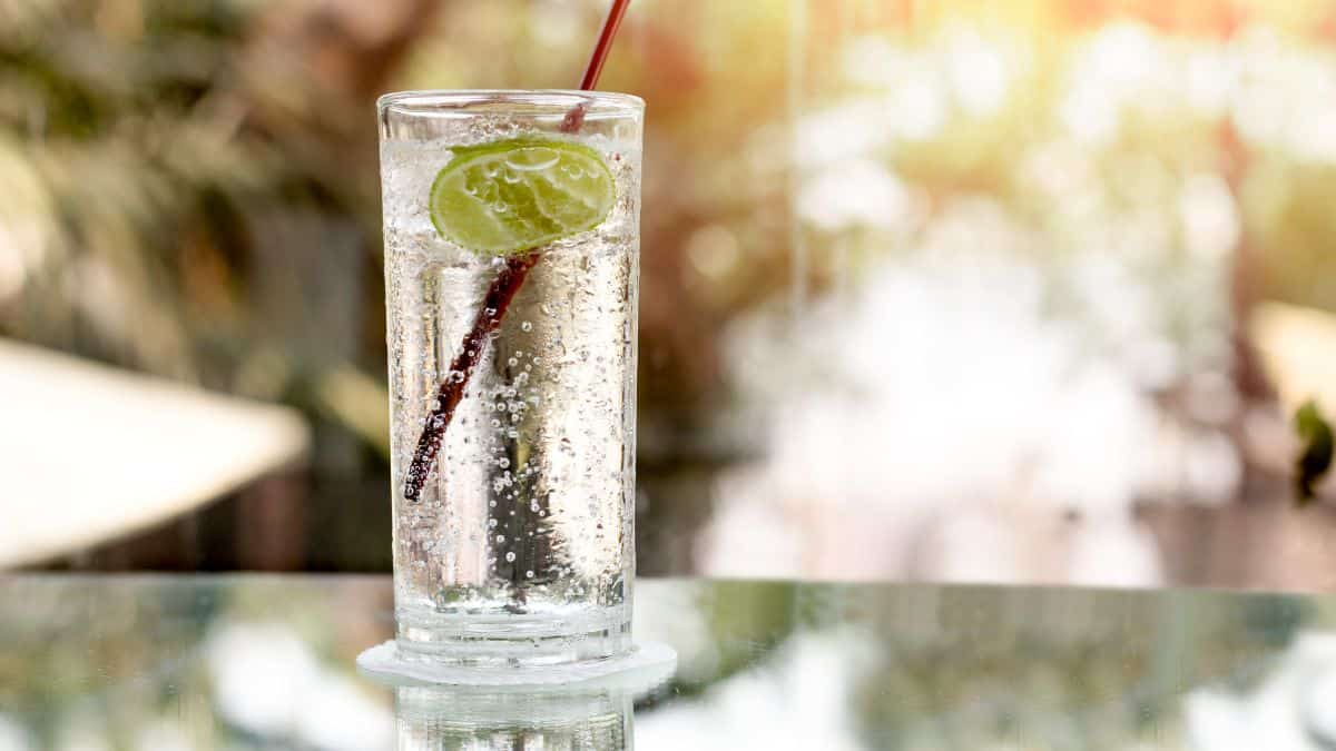 A glass of sparkling water with a lime slice and a straw on a sunny day.