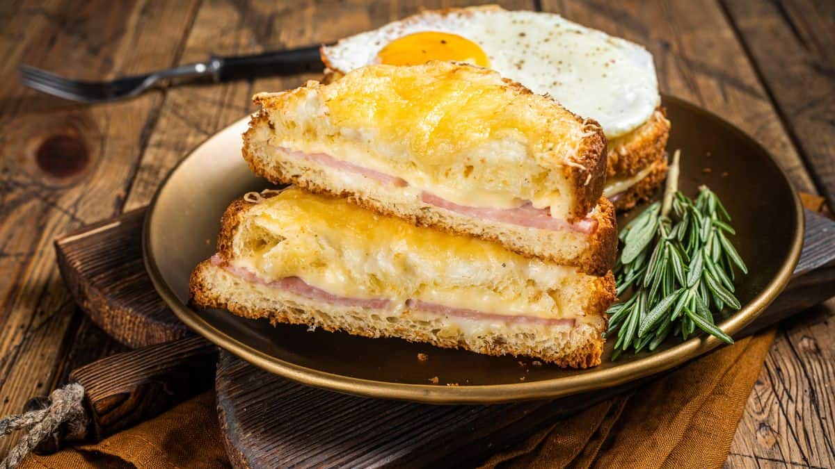 A croque monsieur sandwich with melted cheese and a fried egg on top, served on a wooden table.