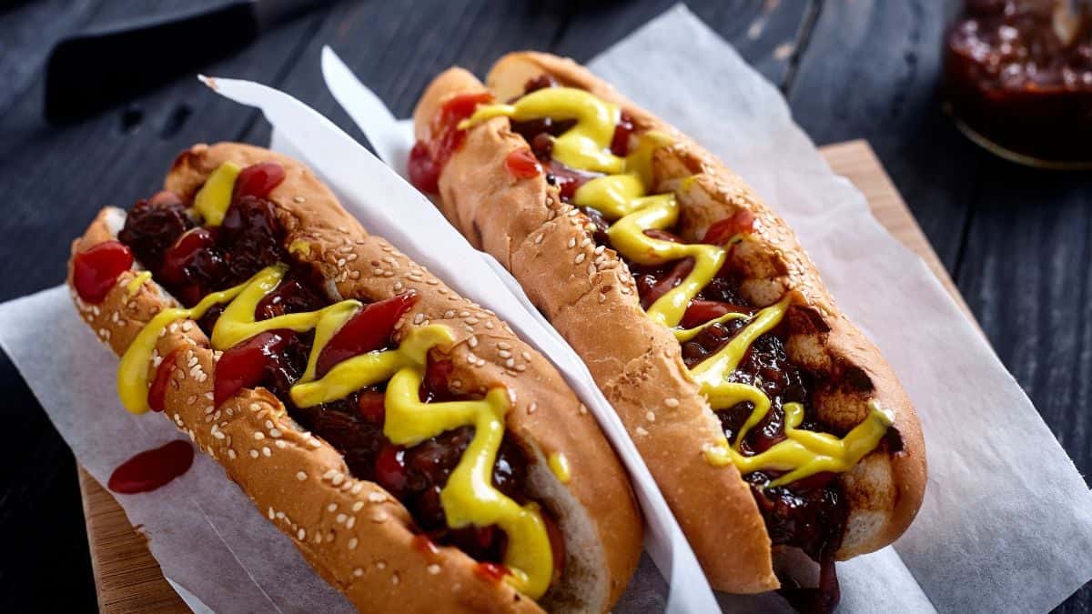 Three hot dogs with mustard and ketchup on a wooden surface.