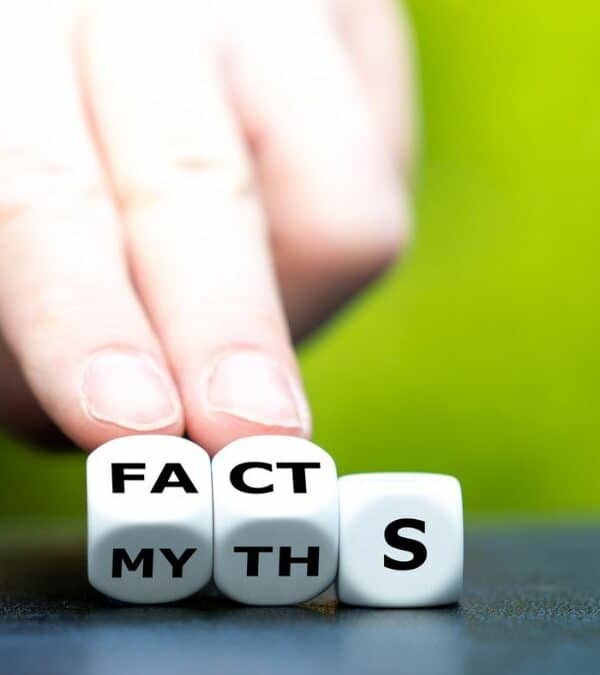 A hand arranging dice that spell "facts" over "myth" against a blurry green background.
