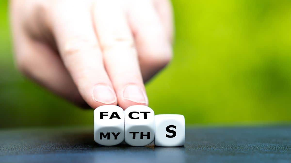 A hand arranging dice that spell "facts" over "myth" against a blurry green background.