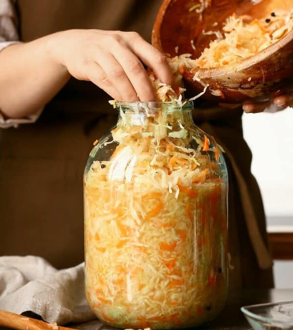 Person preparing homemade sauerkraut by packing shredded cabbage into a glass jar.