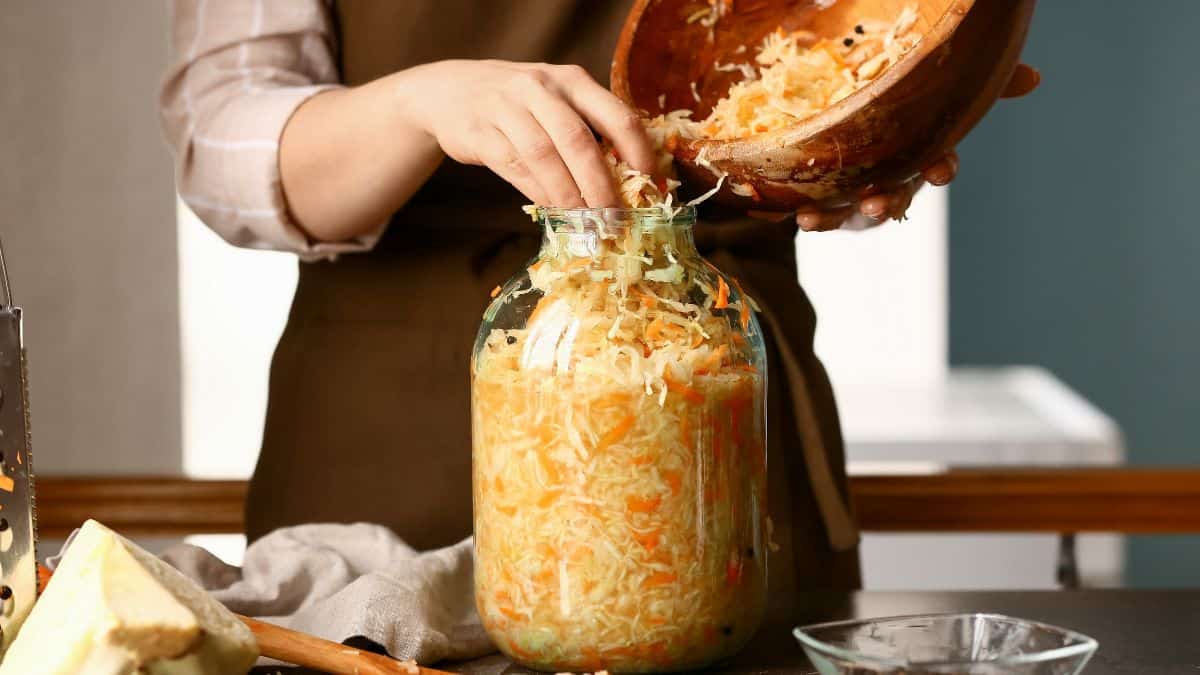 Person preparing homemade sauerkraut by packing shredded cabbage into a glass jar.