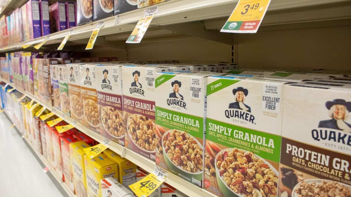 Shelves stocked with assorted varieties of quaker granola cereal in a grocery store aisle.