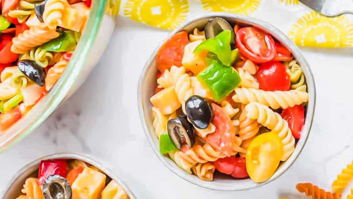 Two bowls of colorful pasta salad with tomatoes, olives, and green bell peppers.