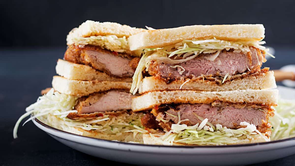 A cutlet sandwich with a side of coleslaw on a white plate.