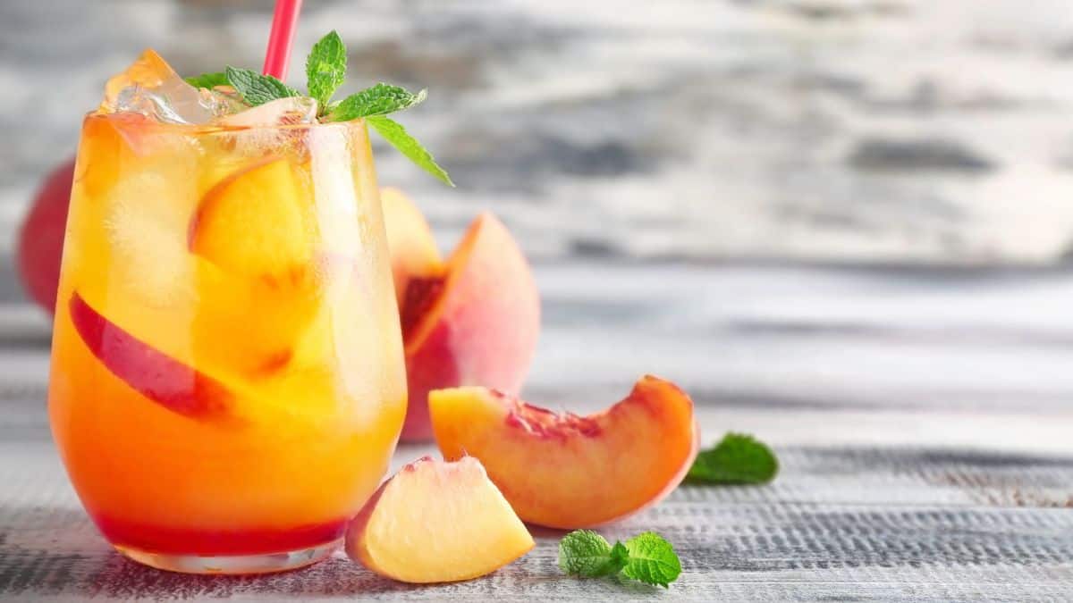 A refreshing glass of peach iced tea, a healthier way to drink alcohol, garnished with fresh peach slices and mint on a rustic table.