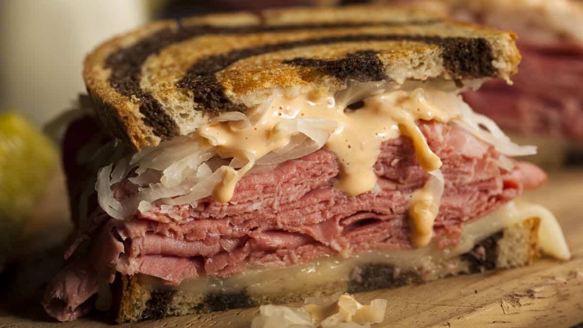 A reuben sandwich with layers of corned beef, sauerkraut, swiss cheese, and thousand island dressing on rye bread.