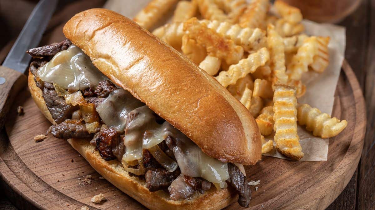 Cheesesteak sandwich with melted cheese and grilled onions, served with a side of crinkle-cut fries.