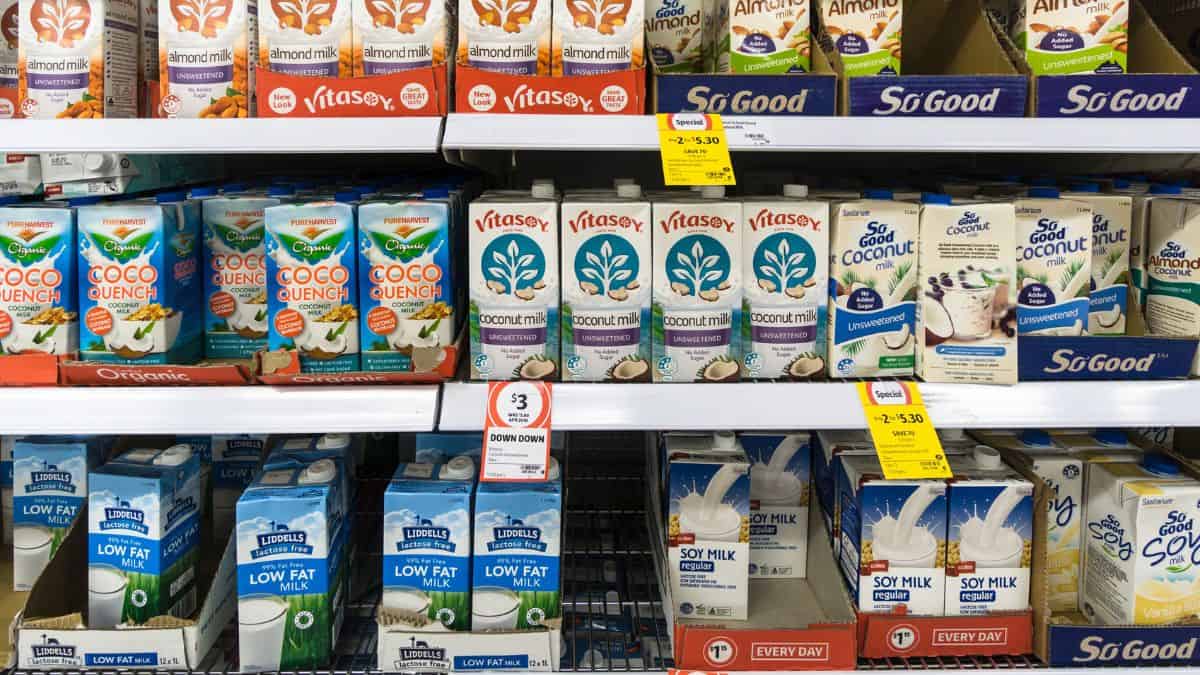 Variety of plant-based milk alternatives on a supermarket shelf, including almond, coconut, and soy milk brands.