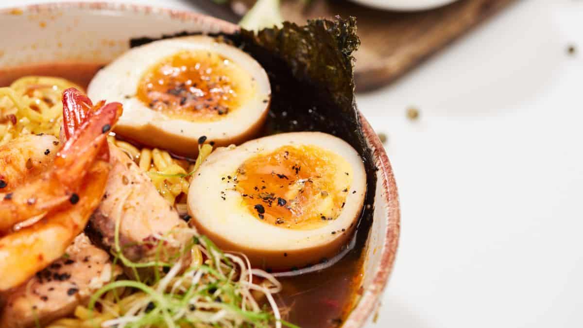 Close-up of a bowl of ramen with soft-boiled egg, shrimp, and garnishes.