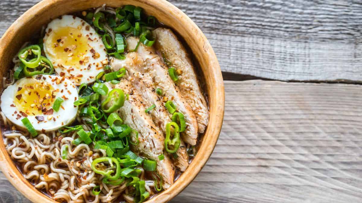 Bowl of ramen with a soft-boiled egg, sliced chicken, green onions, and chili flakes.