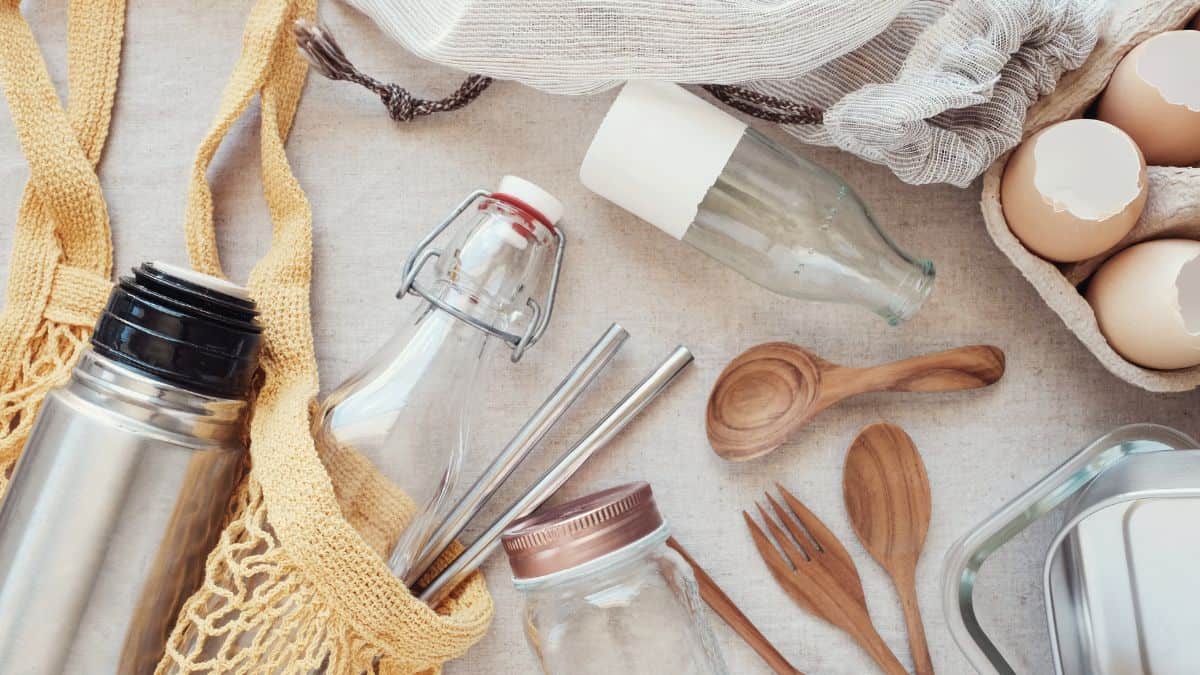 Assorted reusable items including glass bottles, wooden utensils, fabric bags, and metal containers arranged on a light surface.