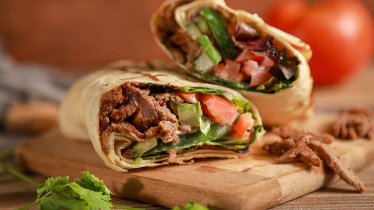 A halved beef wrap with fresh vegetables on a wooden cutting board.