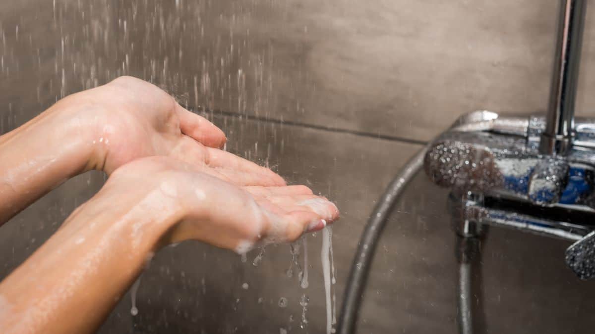A person washing their hands under running water from a stainless steel faucet.