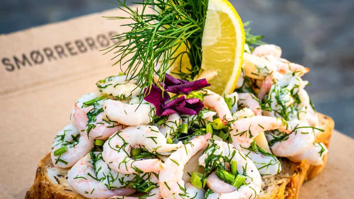 A shrimp sm&oslash;rrebr&oslash;d garnished with dill, lemon, and edible flowers on a wooden board.