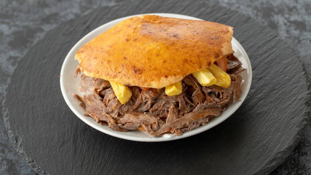 A traditional venezuelan arepa stuffed with shredded beef and plantain chips on a white plate.