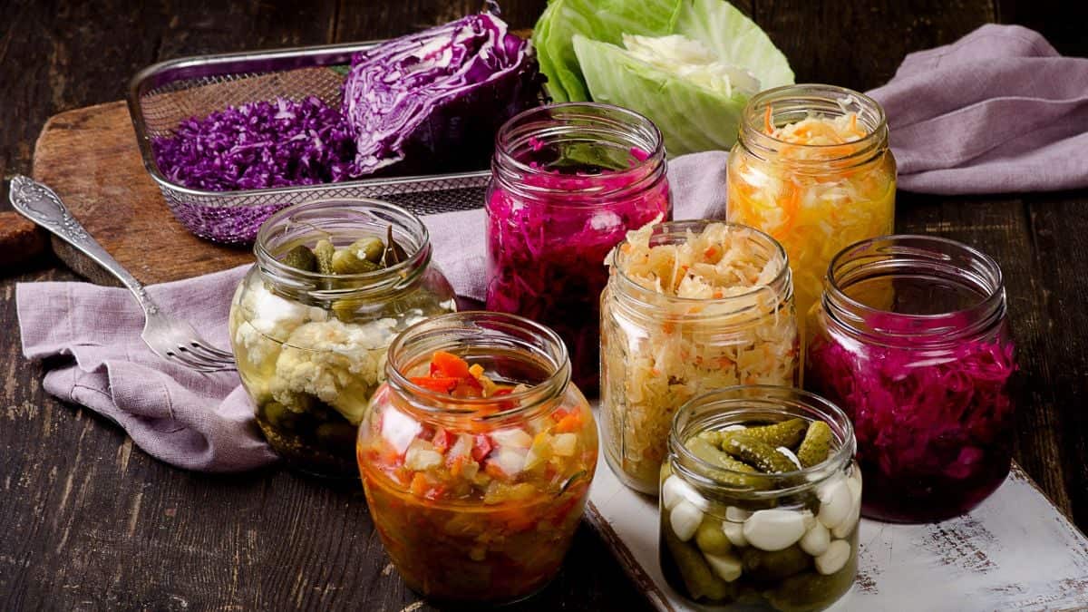 Assorted pickled vegetables in glass jars on a wooden surface.