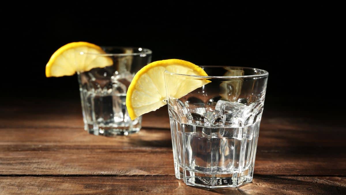 Two glasses with ice cubes and lemon slices on a wooden surface against a dark background.