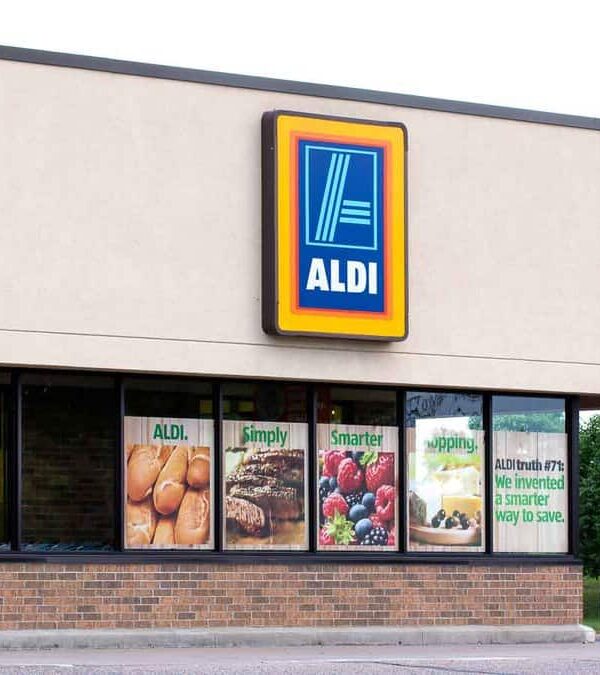 Exterior view of an aldi supermarket featuring large window displays with images of fresh produce and promotional signs.