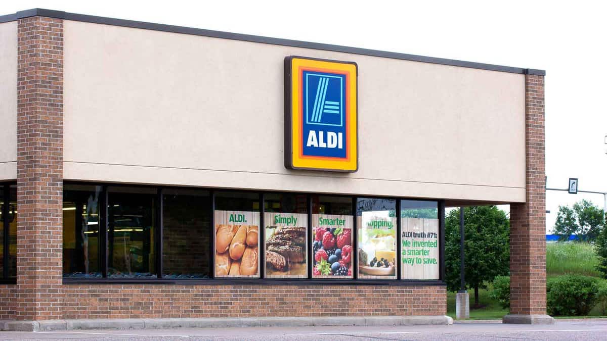 Exterior view of an aldi supermarket featuring large window displays with images of fresh produce and promotional signs.