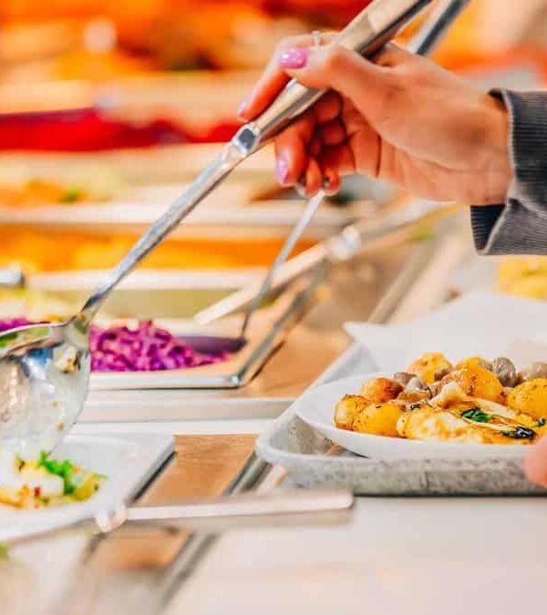 Person serving themselves food at a buffet station.