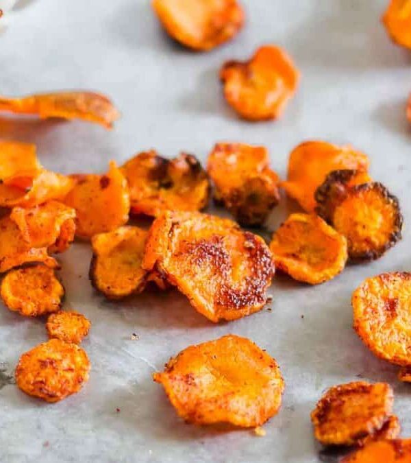 Roasted carrot slices on parchment paper, showing a range of sizes and degrees of charring. some pieces are deeply caramelized.