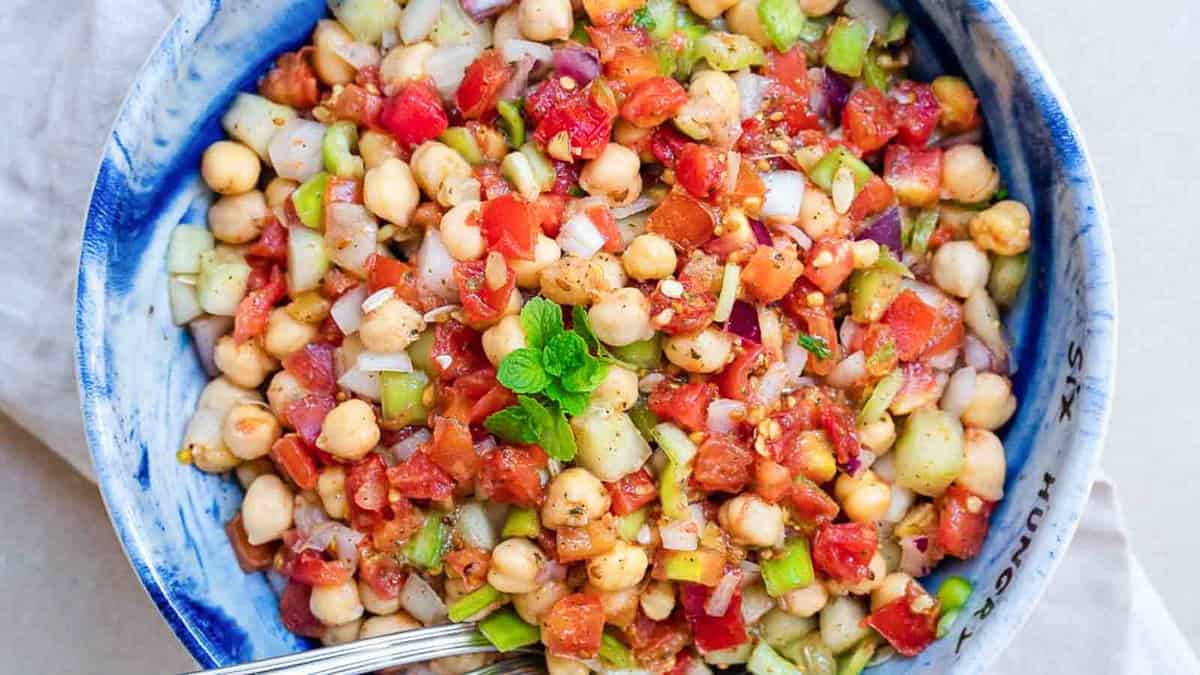 A colorful bowl of chickpea salad with tomatoes, cucumbers, and onions.