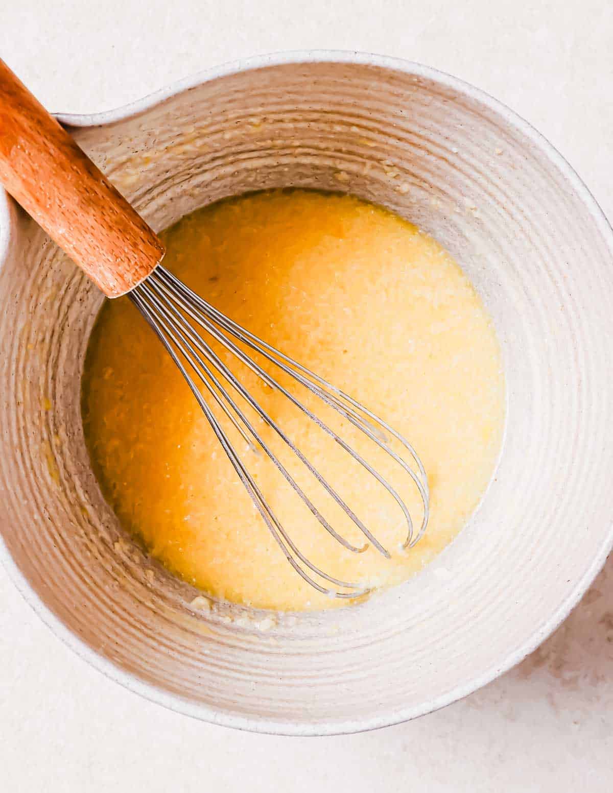 A whisk mixing eggs in a stone bowl, creating a smooth, yellow mixture.