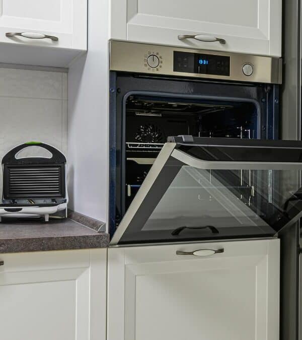Modern kitchen with white cabinets, featuring an open oven, a coffee machine, and a toaster on the countertop.