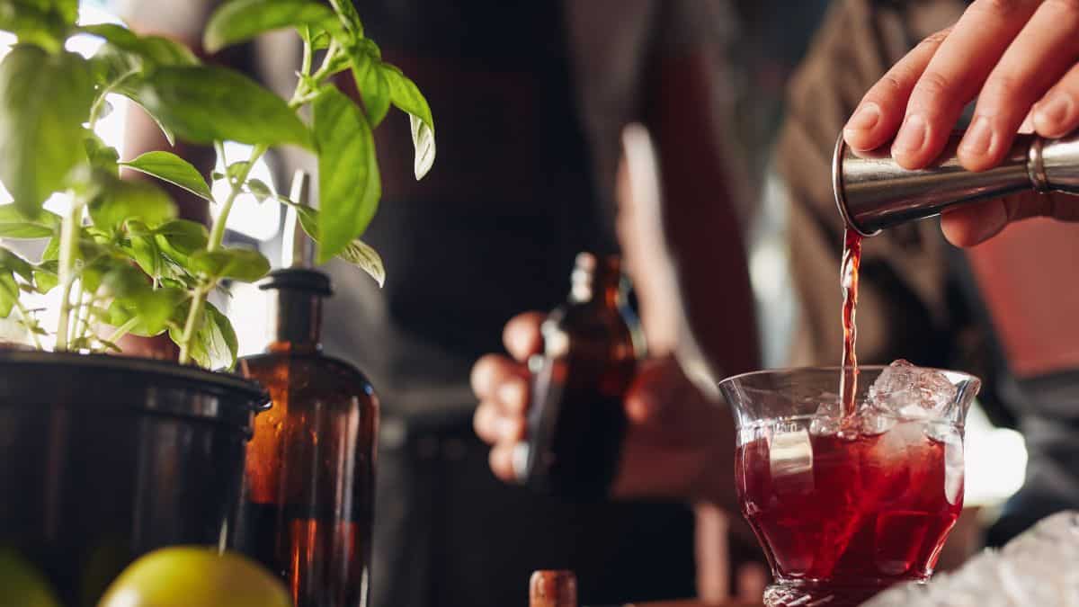 Person pouring a drink into a glass with ice cubes at a bar.