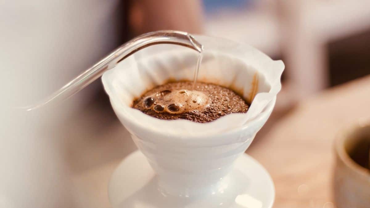 Pouring hot water over ground coffee in a white ceramic pour-over brewer.