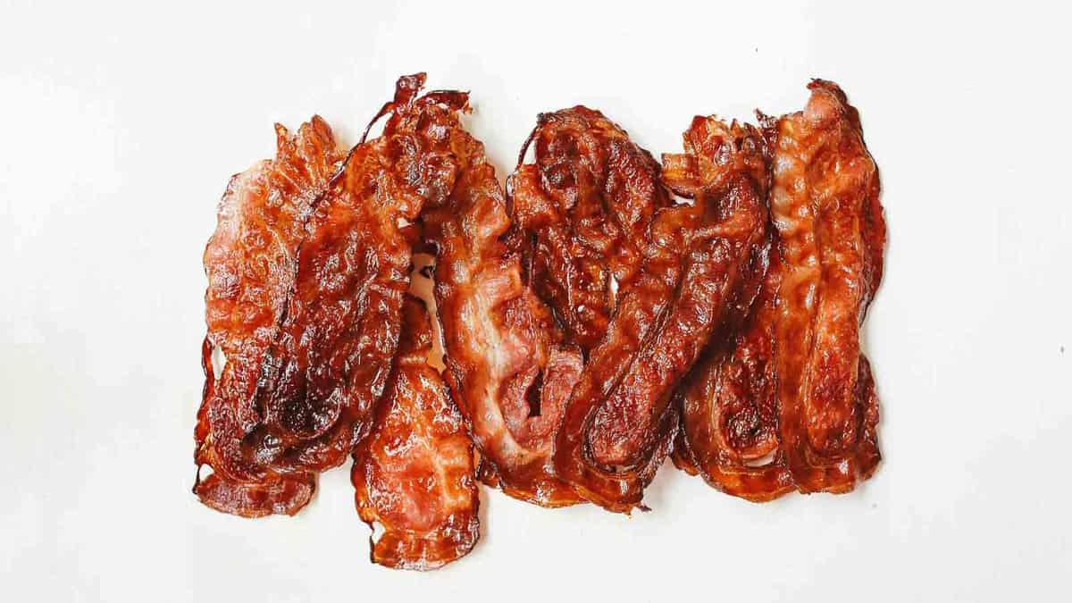 Five strips of crispy bacon arranged side by side on a plain white background.