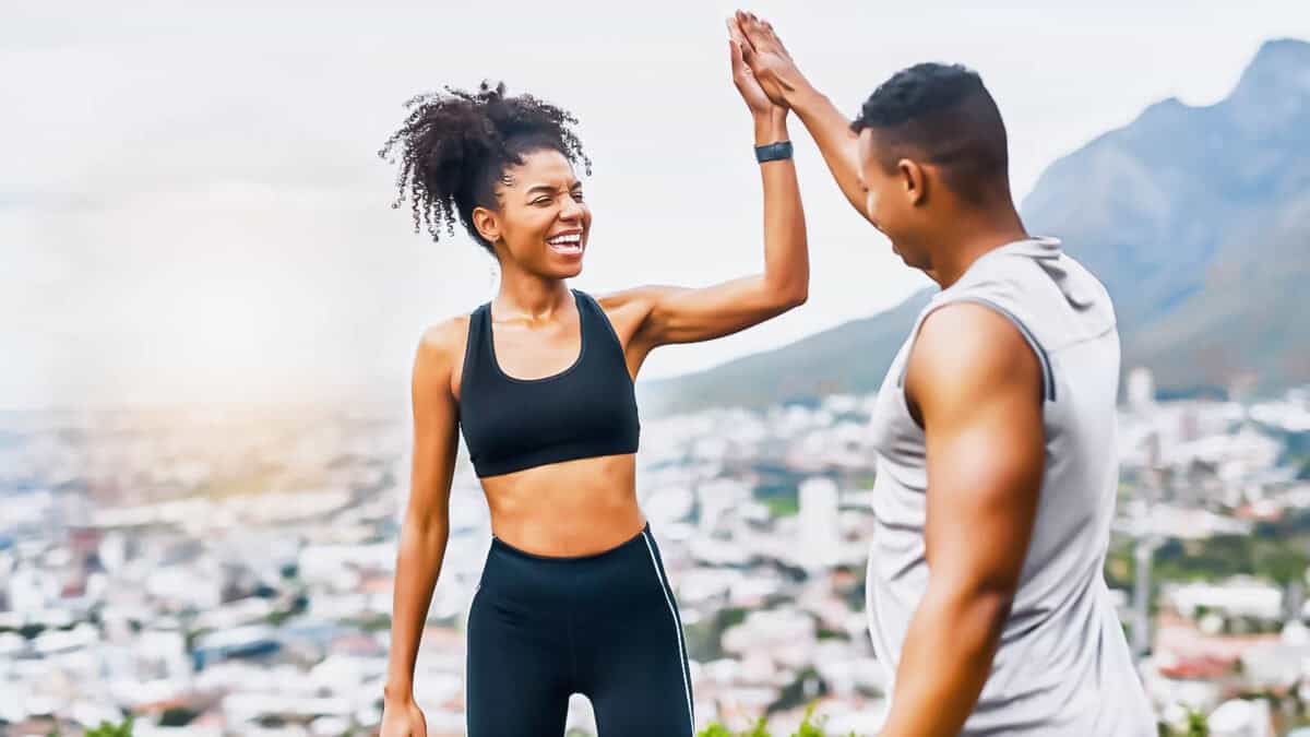 A joyful woman high-fiving a man during an outdoor workout with a city and mountains in the background.