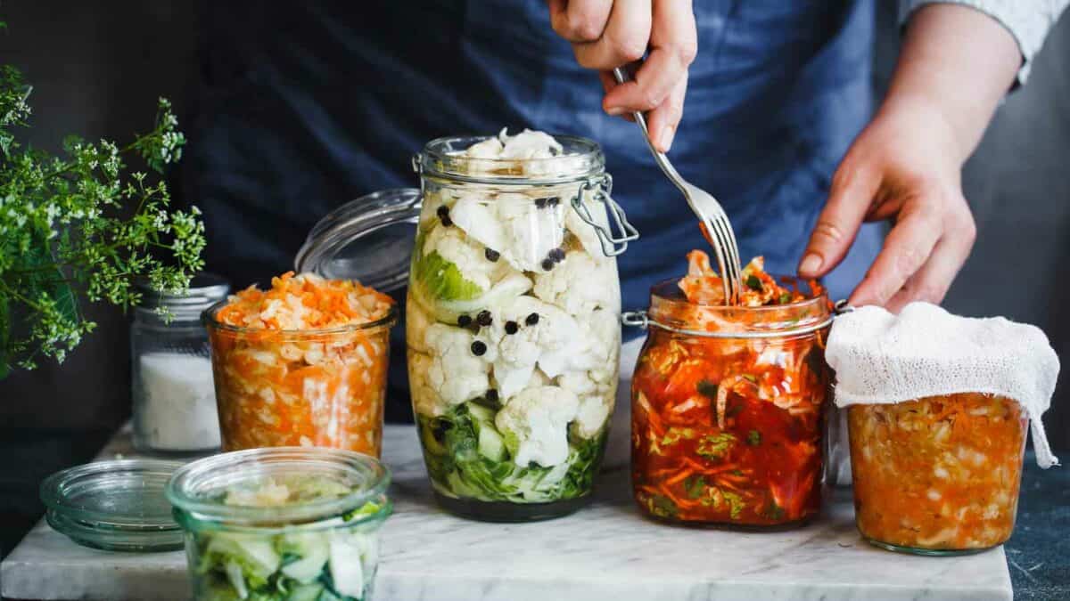 Person preparing various vegetables for fermentation in glass jars.