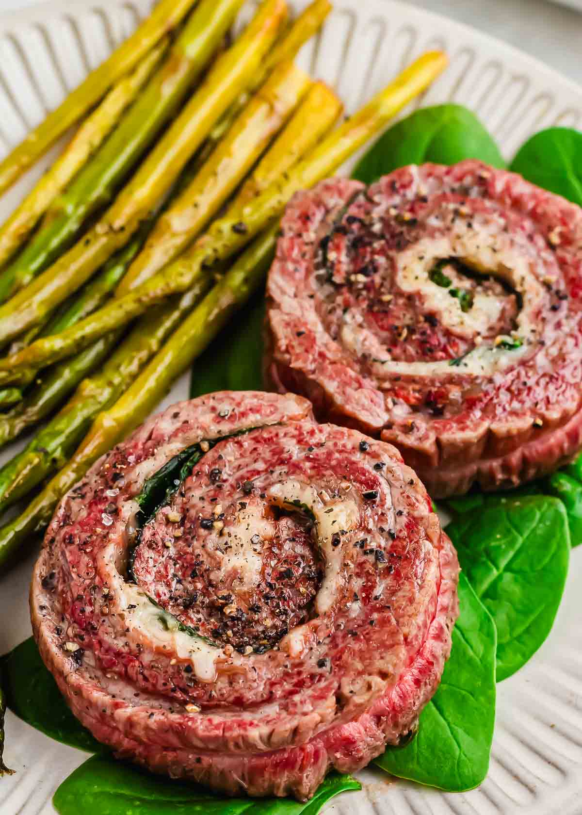Cooked pinwheel steaks and asparagus served on a bed of spinach leaves.