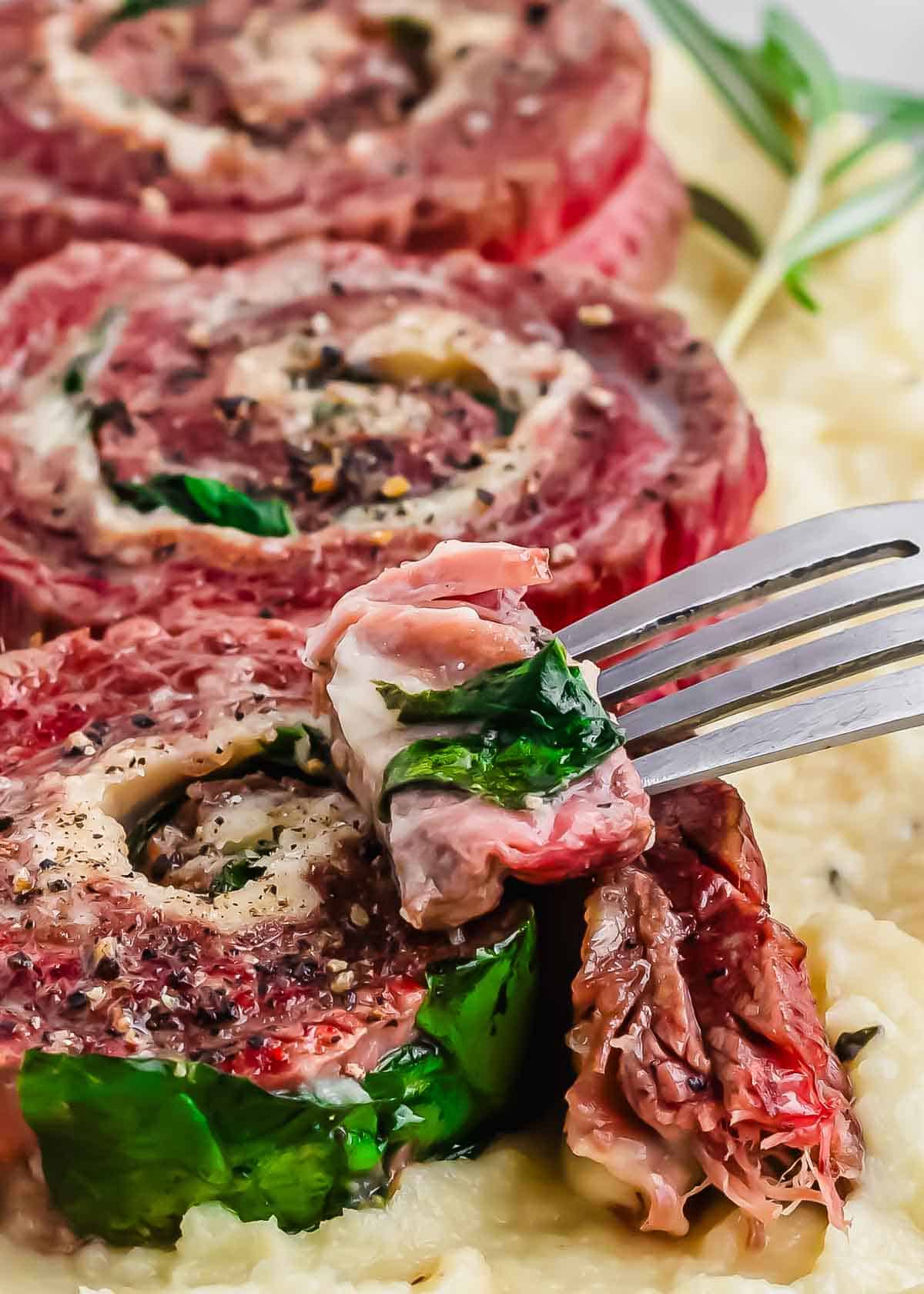 Sliced stuffed pinwheel flank steaks on a bed of mashed parsnips with a piece being lifted on a fork.