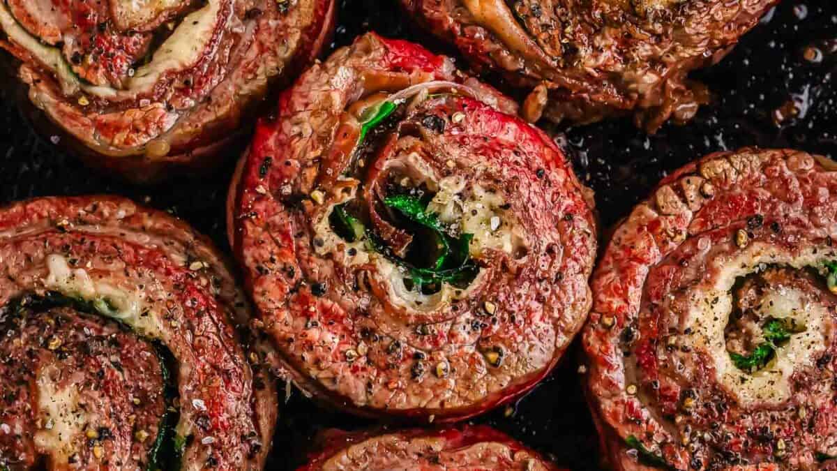 Flank steak pinwheels seasoned with herbs and spices in a skillet.
