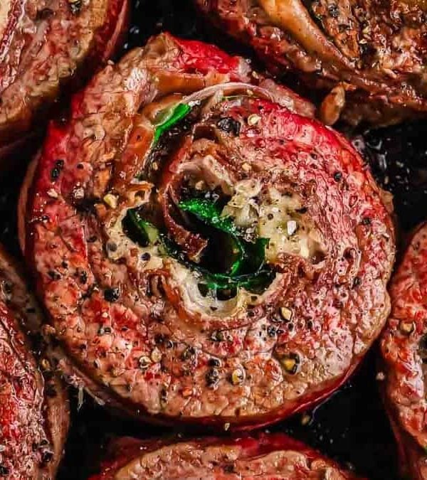 Flank steak pinwheels seasoned with herbs and spices in a skillet.