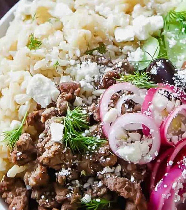 A plate of greek gyros with rice, cucumber, feta cheese, olives, red onions, and dill, accompanied by a fork on the side.