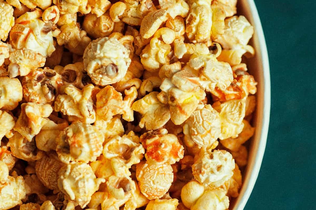 Close-up view of a bowl filled with caramel popcorn on a green background, illustrating how to make flavored popcorn.