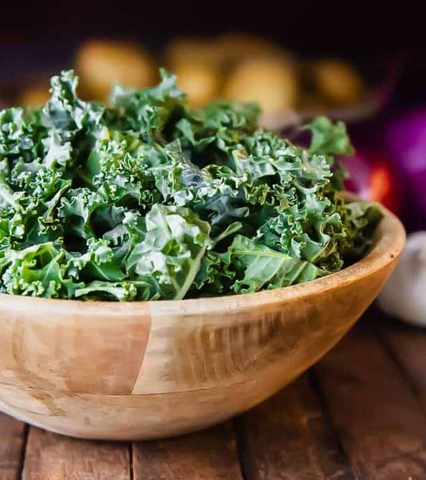 Fresh chopped kale in wooden bowls with garlic and other ingredients in the background