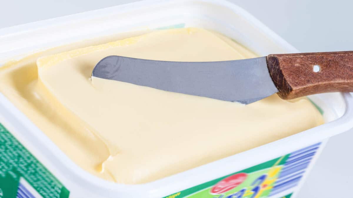 A butter knife with a wooden handle rests on a margarine container, with some margarine on the knife blade.