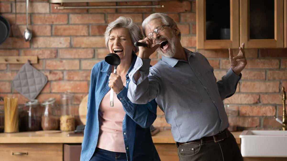 An elderly couple singing and having fun in the kitchen with a ladle as a microphone.