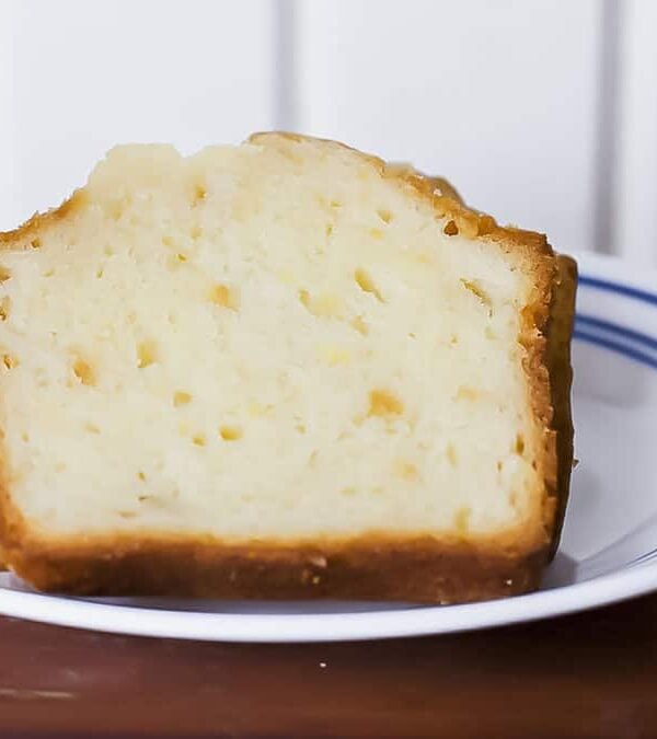 A slice of lemon pound cake on a white plate with blue stripes, placed on a wooden table.